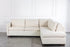Beige sectional sofa bed in a minimalistic room with white walls and gray floor.