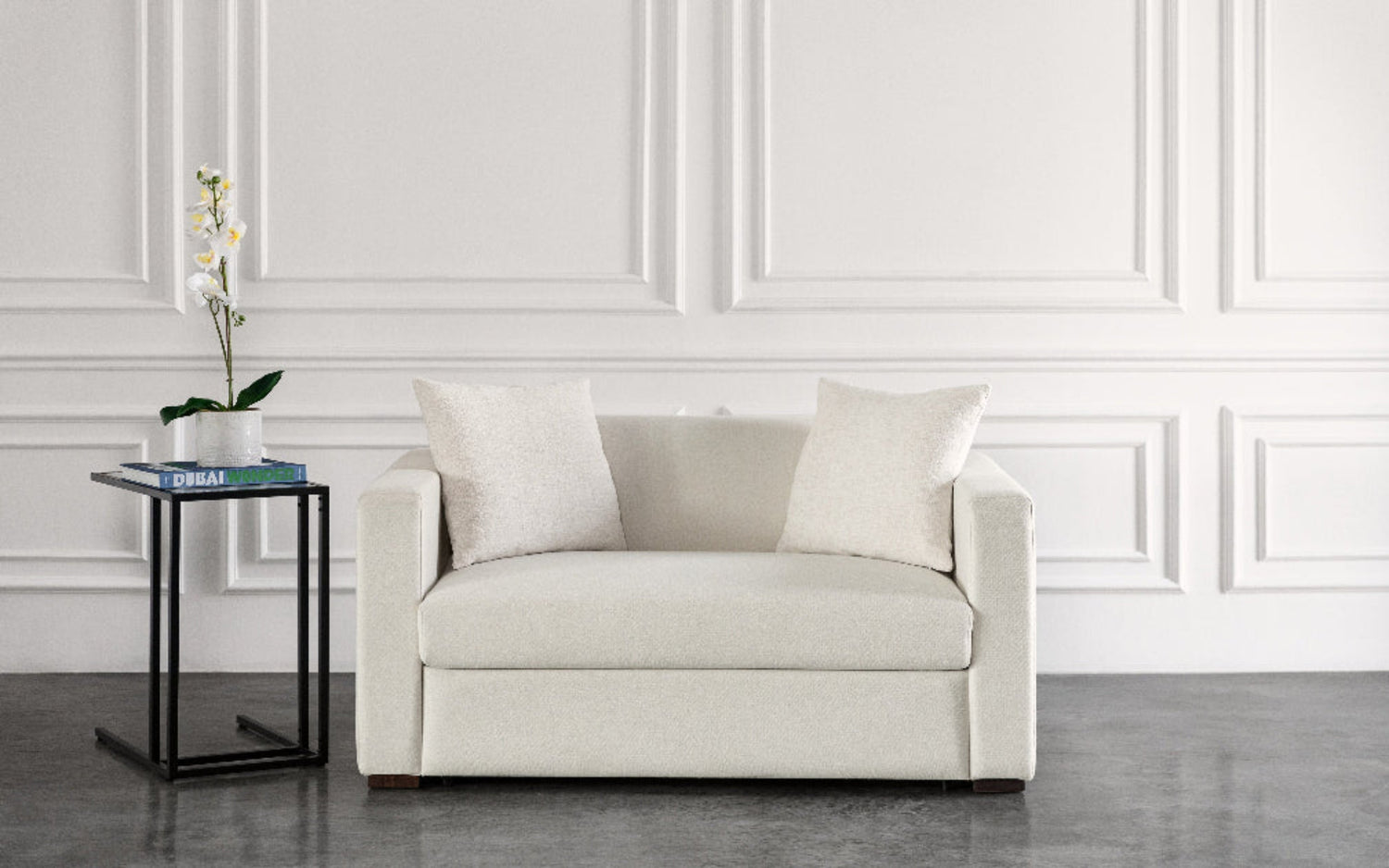 Beige armchair sofa bed in a room with a white wall and a small table with decor items.