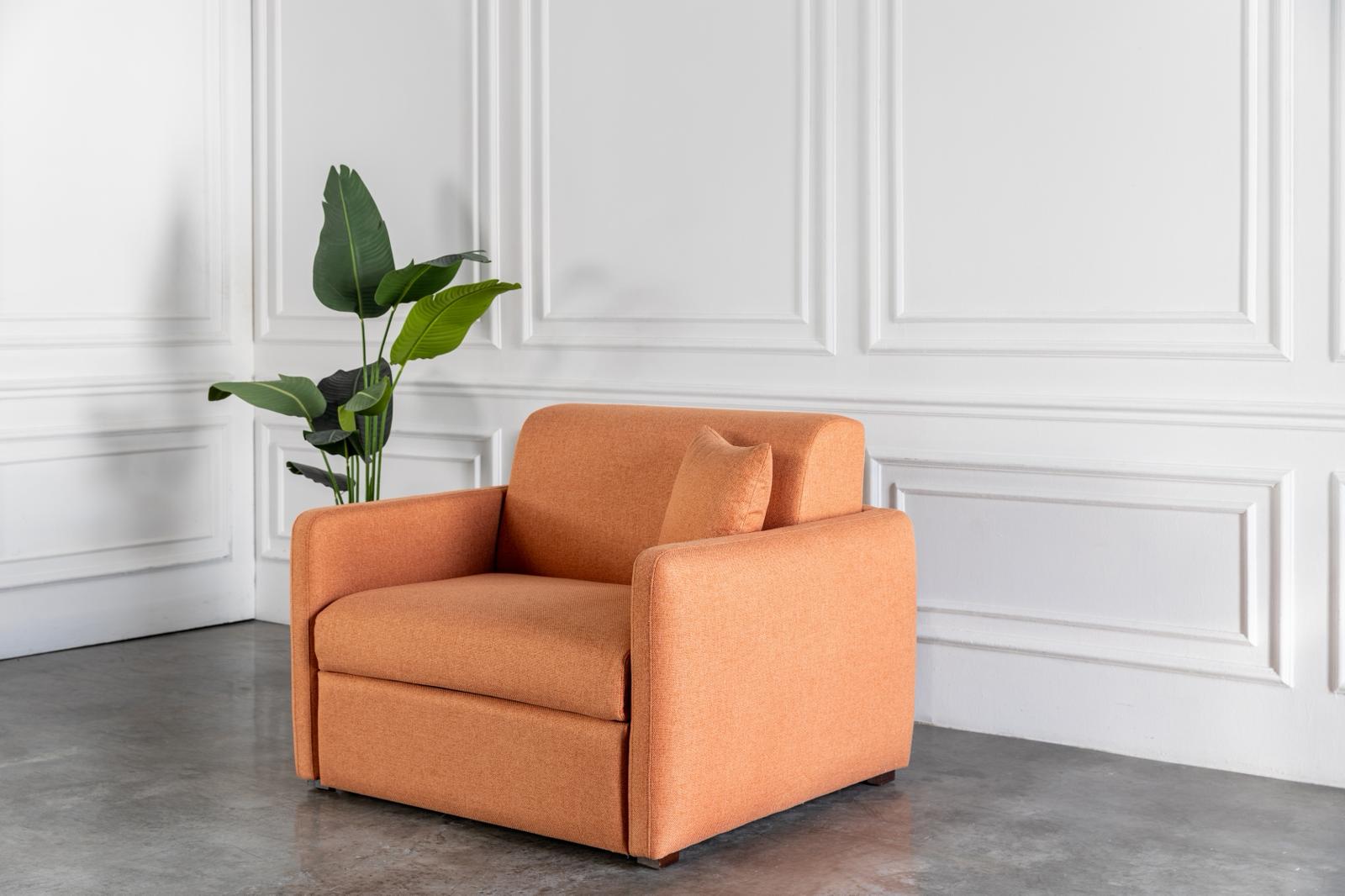Orange comeover armchair sofa bed in a room with white paneled walls and a plant