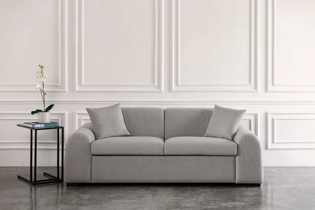 Gray sofa bed in a room with white walls and a small table with a plant.