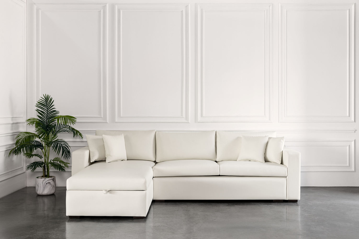 White sectional sofa bed in a room with a plant and decorative wall.